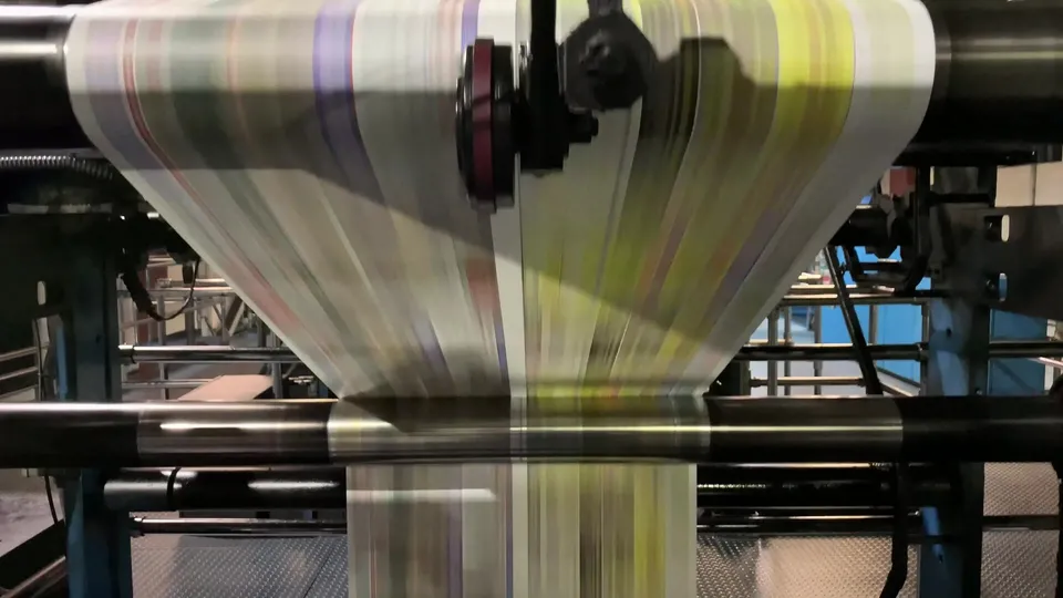 A printing press running at speed, paper flying through the rollers
